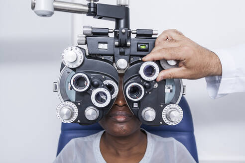 Optometrist, der die optometrische Ausrüstung während der Untersuchung der Sehkraft einer schwarzen Frau einstellt - ADSF28784