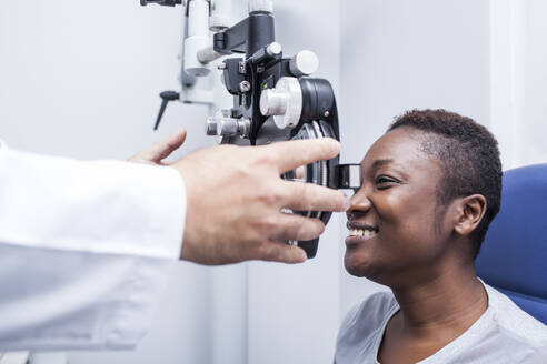 Optometrist adjusting the optometry equipment during study of the eyesight of a happy black woman - ADSF28785