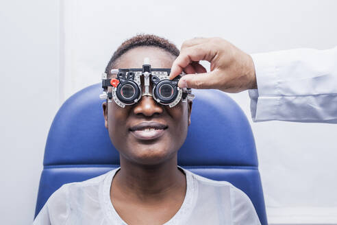Optometrist, der die optometrische Ausrüstung während der Untersuchung der Sehkraft einer schwarzen Frau einstellt - ADSF28787