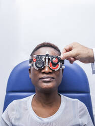 Optometrist, der die optometrische Ausrüstung während der Untersuchung der Sehkraft einer schwarzen Frau einstellt - ADSF28788