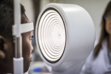 Schwarze Frau in der Optometriekabine bei der Untersuchung des Sehvermögens mit einem modernen Hornhauttopografen - ADSF28791