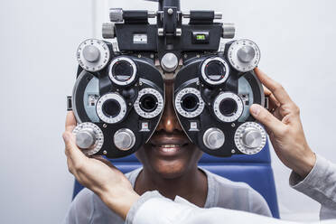 Optometrist, der die optometrische Ausrüstung während der Untersuchung der Sehkraft einer schwarzen Frau einstellt - ADSF28793