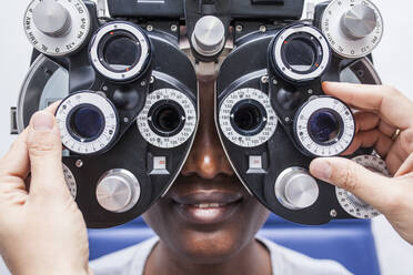 Optometrist, der die optometrische Ausrüstung während der Untersuchung der Sehkraft einer schwarzen Frau einstellt - ADSF28794
