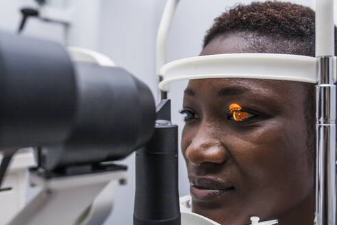 Optometrist adjusting the retinograph during study of the eyesight of a black woman - ADSF28795