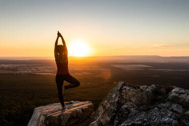 Junge Yogi Frau übt Yoga auf einem Felsen in den Bergen mit dem Licht des Sonnenaufgangs, Rückenansicht mit einem Bein und Arme angehoben - ADSF28799