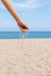 Anonyme Frau mit einer Handvoll Sand in den Fingern, die im Sommer am Meer steht - ADSF28811