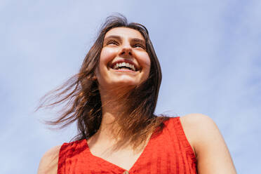 Low angle of cheerful female standing on background of blue cloudy sky - ADSF28816