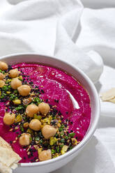 From above appetizing beetroot hummus garnished with chickpea served on fabric background with bread - ADSF28833