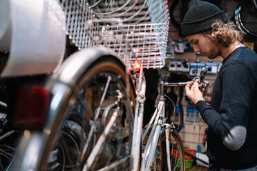 Seitenansicht eines beschäftigten männlichen Meisters, der ein Fahrrad repariert, während er in einer schäbigen Reparaturwerkstatt arbeitet - ADSF28835