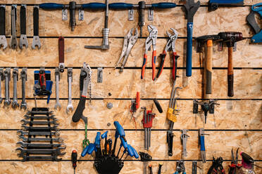 Various metal tools hanging in rows on wooden wall in shabby bicycle repair service - ADSF28840