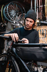 Serious male mechanic fixing handlebar of bicycle while working in repair service workshop - ADSF28841