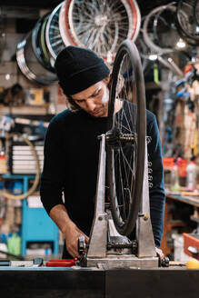 Junger männlicher Meister, der den Reifen eines Fahrrads bei der Arbeit in einer professionellen Reparaturwerkstatt untersucht - ADSF28844