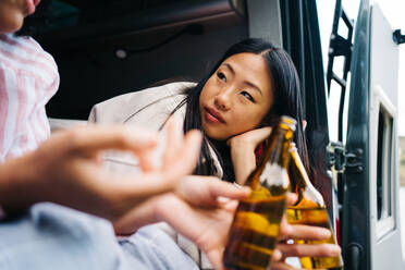 Junge gemischtrassige Frauen trinken Bier, während sie während einer Sommerreise gemeinsam im Wohnmobil chillen - ADSF28860