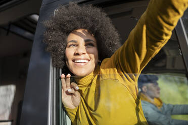 Aufgeregte afroamerikanische Reisende, die lächelt und ein Selfie macht, während sie aus dem Fenster eines Lieferwagens in der Nähe ihres Freundes blickt - ADSF28942