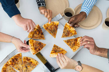 From above of company of crop anonymous multiethnic friends gathering at table and eating delicious pizza - ADSF28981