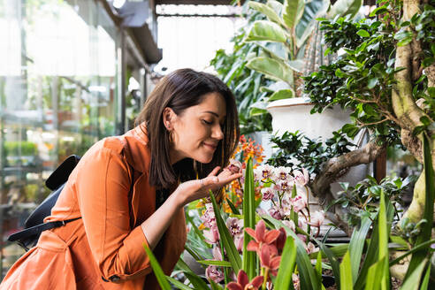 Side view of delighted female customer picking blossoming potted flowers in garden market - ADSF28990