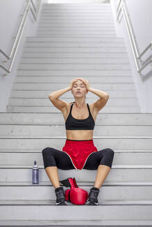 Female boxer with head in hands sitting on staircase - EAF00084