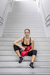 Selbstbewusste junge Sportlerin auf einer Treppe im Keller sitzend - EAF00086