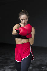 Weibliche Athletin mit Boxhandschuhen beim Training im Keller - EAF00091