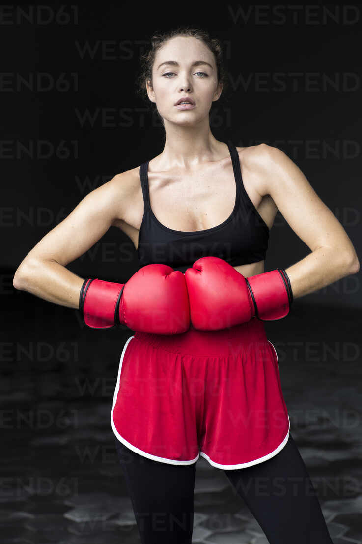 Portrait of confident young woman wearing red boxing gloves and