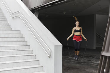 Sportswoman skipping with rope by staircase - EAF00098