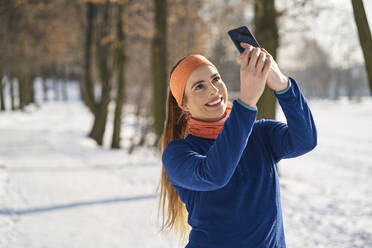 Lächelnde junge Frau nimmt Selfie durch Smartphone im Winter - BSZF01912