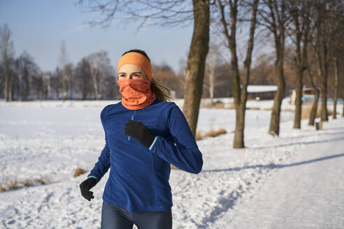 Woman wearing gaiter face mask while running during winter - BSZF01915