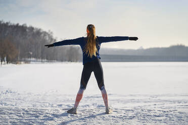 Frau beim Sport mit ausgestreckten Armen im Schnee im Winter - BSZF01918