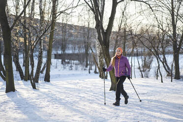 Frau mit Wanderstock, die im Winter im Schnee läuft - BSZF01928