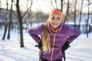 Glückliche junge Frau mit Wanderstöcken im Winter - BSZF01930