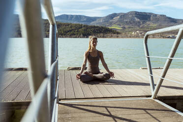 Young woman meditating on jetty - OCAF00695