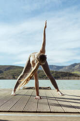 Active woman doing Triangle pose on jetty - OCAF00698