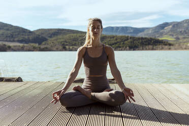 Frau mit geschlossenen Augen beim Meditieren im Lotussitz an einem sonnigen Tag - OCAF00700