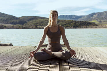 Woman with eyes closed meditating while sitting in lotus position on sunny day - OCAF00700