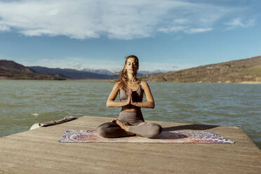 Junge Frau mit verschränkten Händen beim Meditieren an einem sonnigen Tag - OCAF00705