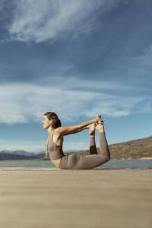 Junge Frau übt Dhanurasana auf dem Bootssteg - OCAF00708