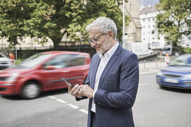 Bärtiger Geschäftsmann benutzt Mobiltelefon auf der Straße - RORF02825