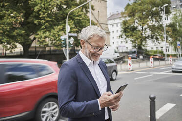 Smiling male professional using smart phone on road - RORF02826