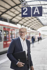 Männlicher Berufstätiger schaut weg, während er einen Laptop am Bahnhof hält - RORF02831