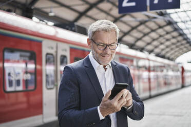 Männlicher Berufstätiger, der auf dem Bahnsteig stehend ein Mobiltelefon benutzt - RORF02834