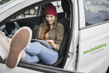 Lächelnde junge Frau, die ein digitales Tablet benutzt, während sie im Auto sitzt - RORF02841