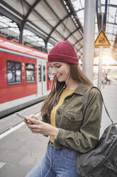 Lächelnde Frau, die ein Mobiltelefon benutzt, während sie auf einem Bahnsteig steht - RORF02842