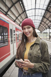 Lächelnde schöne Frau mit Mobiltelefon am Bahnhof - RORF02844