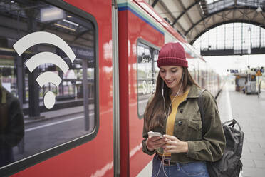 Lächelnde Frau, die im Zug am Bahnhof ihr Mobiltelefon benutzt - RORF02846