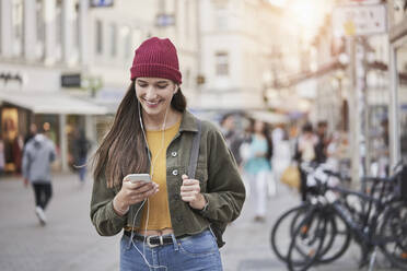 Smiling young woman using mobile phone in city - RORF02850