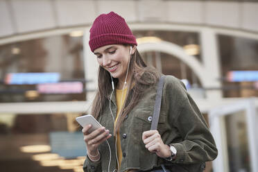 Lächelnde junge Frau mit Mobiltelefon vor einem Gebäude - RORF02853