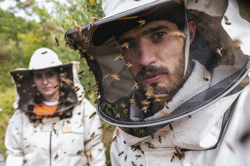 Männlicher und weiblicher Imker mit Honigbienen auf einem Schutzanzug auf einem Bauernhof - JCMF02227