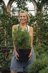Lächelnde Frau mit Topfpflanze vor einem Gewächshaus - VPIF04641