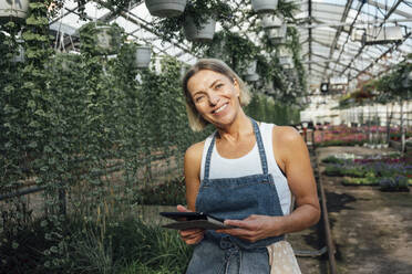 Lächelnde Landarbeiterin mit digitalem Tablet in einer Gärtnerei - VPIF04659