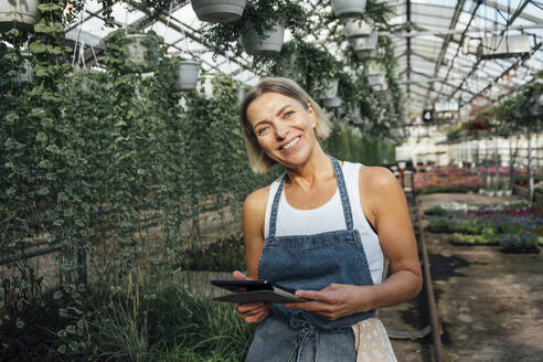 Smiling female agriculture worker holding digital tablet at plant nursery - VPIF04659